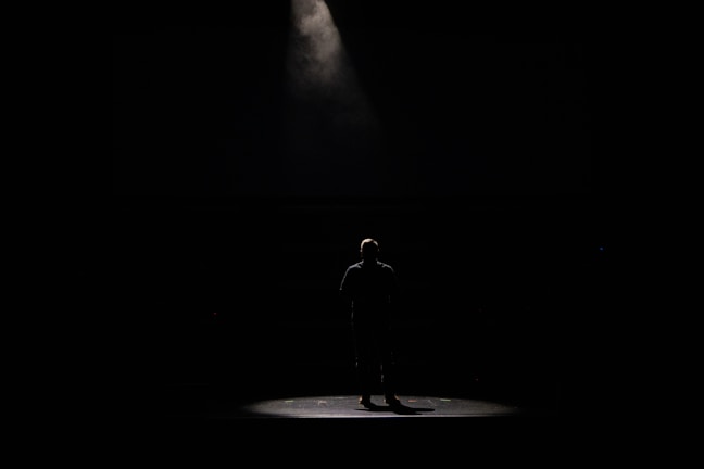 Warm spotlight on Uday Harish rehearsing a monologue in an empty theatre.