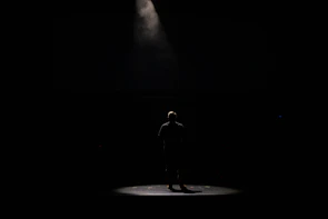 A spotlight illuminating a solo performer mid-song on a dimly lit stage.