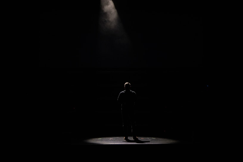 Binoy Cherian performing an intense monologue on stage under warm spotlight.
