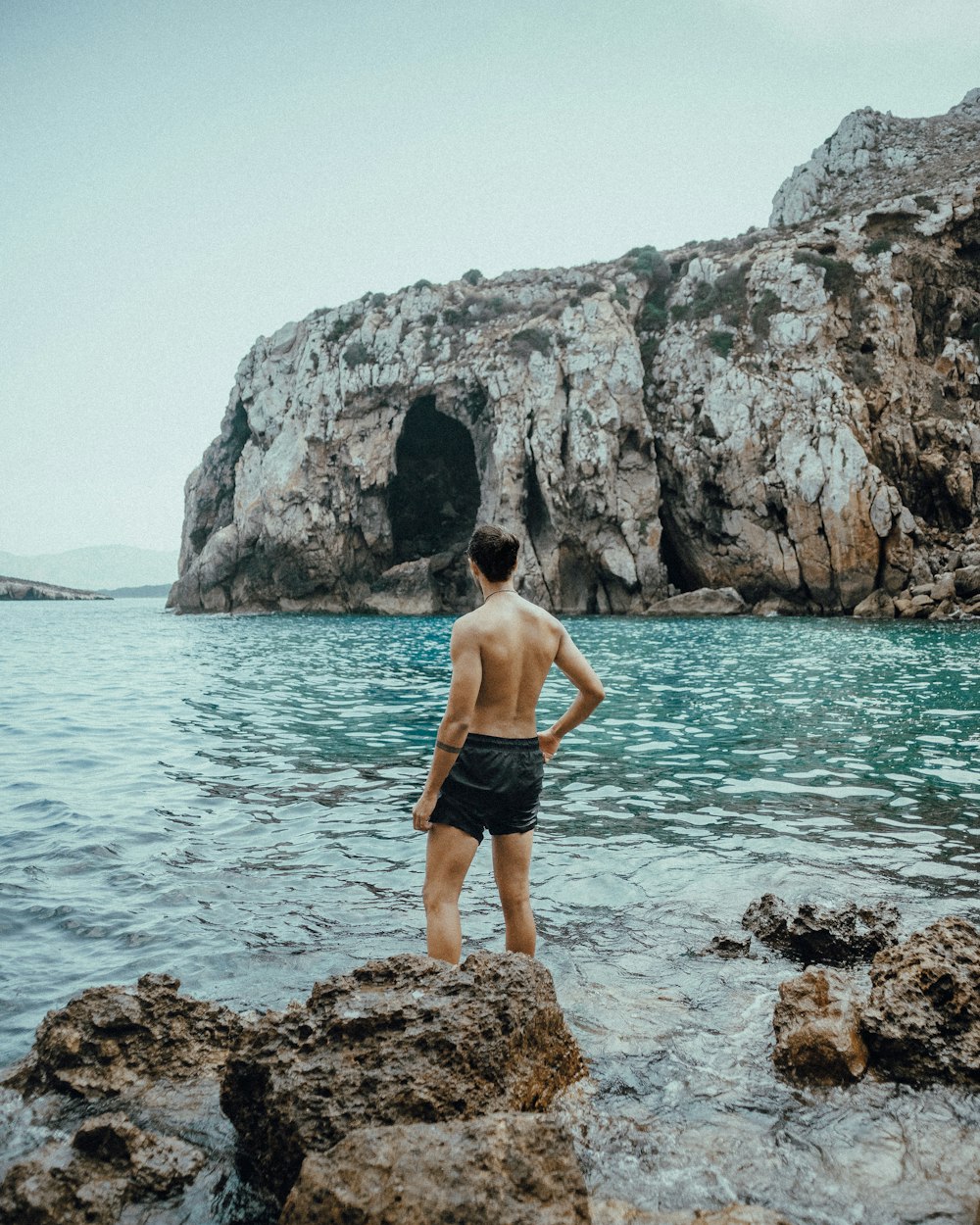 man in black shorts standing on rocky shore during daytime