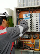 An electrician in a hard hat and face shield testing an electrical panel