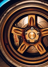 A close-up view of a car's bronze alloy wheel with intricate design detailing and visible brake components, including a Brembo brake caliper.