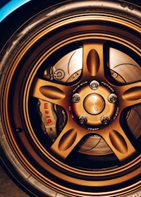 A close-up view of a car's bronze alloy wheel with intricate design detailing and visible brake components, including a Brembo brake caliper.
