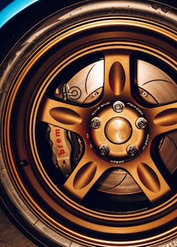 A close-up view of a car's bronze alloy wheel with intricate design detailing and visible brake components, including a Brembo brake caliper.