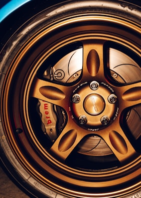 A close-up view of a car's bronze alloy wheel with intricate design detailing and visible brake components, including a Brembo brake caliper.