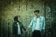 Couple walking hand-in-hand through the courtyard of Masjid al-Haram, with the Kaaba in the background.