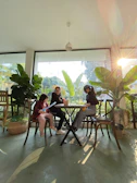 A group sharing stories in a warm, sunlit room filled with plants.