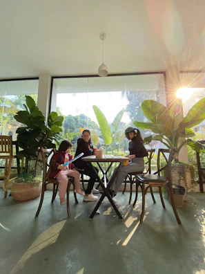 A group sharing stories in a warm, sunlit room filled with plants.