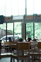 A bright, airy cafe interior featuring natural wood tables and lush green plants.
