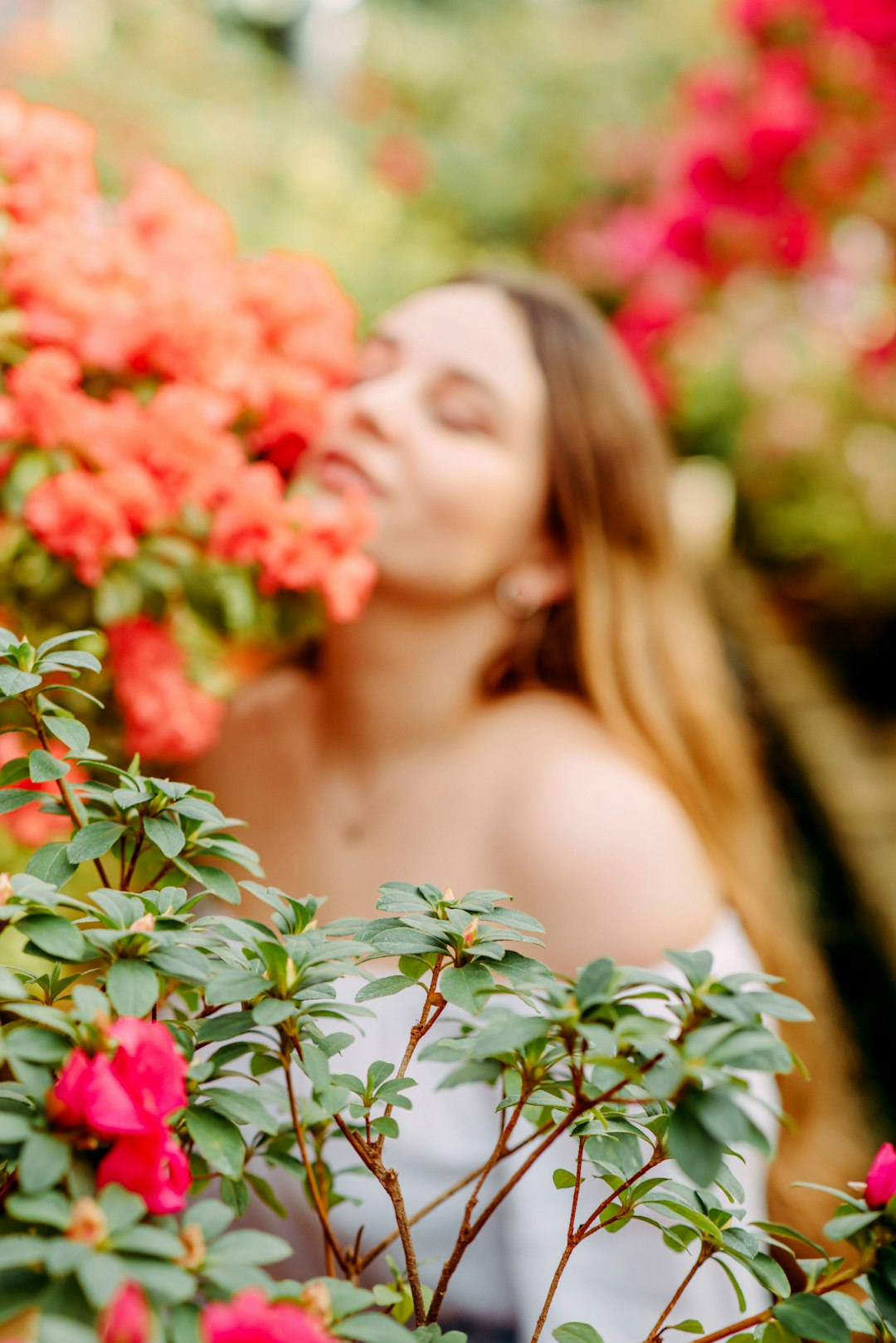 woman in white tank top standing beside red flowers