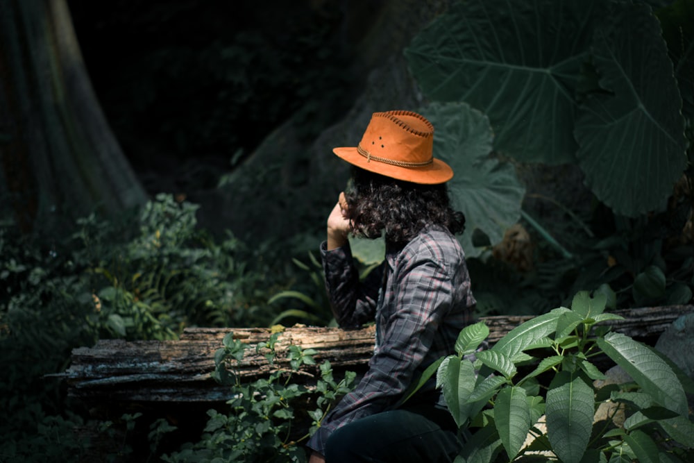 man in grey and black camouflage jacket and orange hat sitting on brown wooden log during