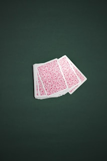 A deck of playing cards is fanned out across a green surface. The backs of the cards are covered with a red geometric pattern.