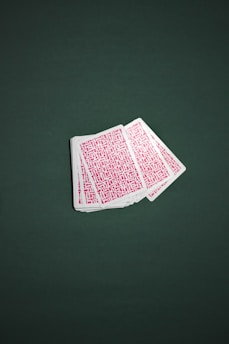 A deck of playing cards is fanned out across a green surface. The backs of the cards are covered with a red geometric pattern.