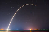 A SpaceX rocket launching into the starry night sky, flames glowing brightly.