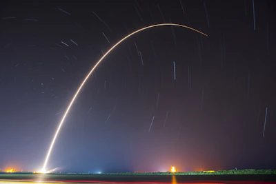 A SpaceX rocket launching into the starry night sky, flames glowing brightly.
