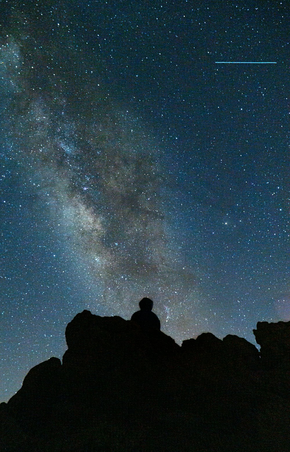 silhouette of man sitting on rock under starry night