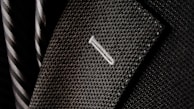 A close-up of a textured suit lapel with detailed stitching, accompanied by a patterned tie in the background.
