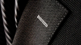 Close-up of a gold-threaded lapel on a black suit jacket, highlighting craftsmanship.