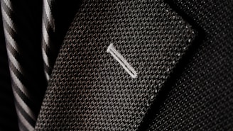 A close-up of a textured suit lapel with detailed stitching, accompanied by a patterned tie in the background.