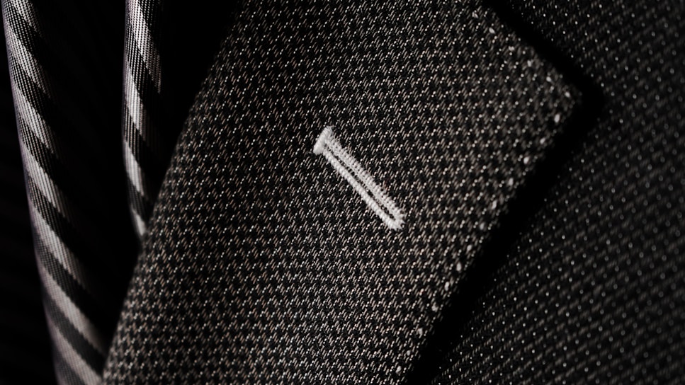 Close-up of handcrafted stitching on a luxurious smart-fit blazer in soft neutral tones.