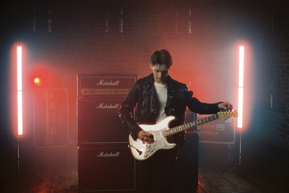 man in black leather jacket playing white stratocaster electric guitar