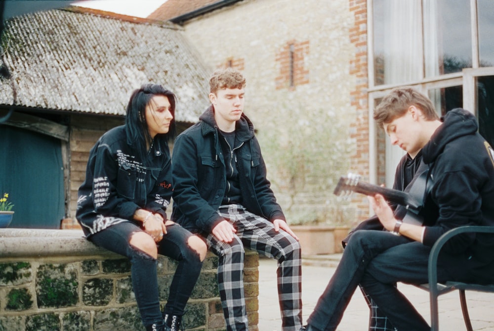 3 men and 2 women sitting on brown brick wall during daytime