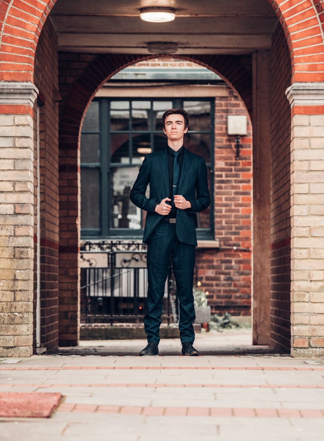 man in black suit standing beside brown brick building during daytime