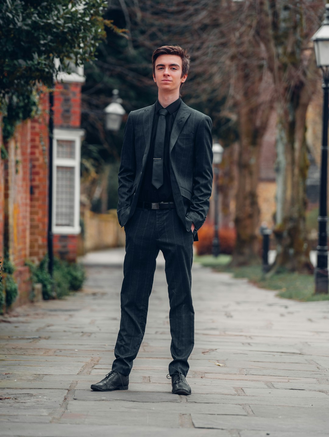 man in black suit jacket and brown pants standing on sidewalk during daytime