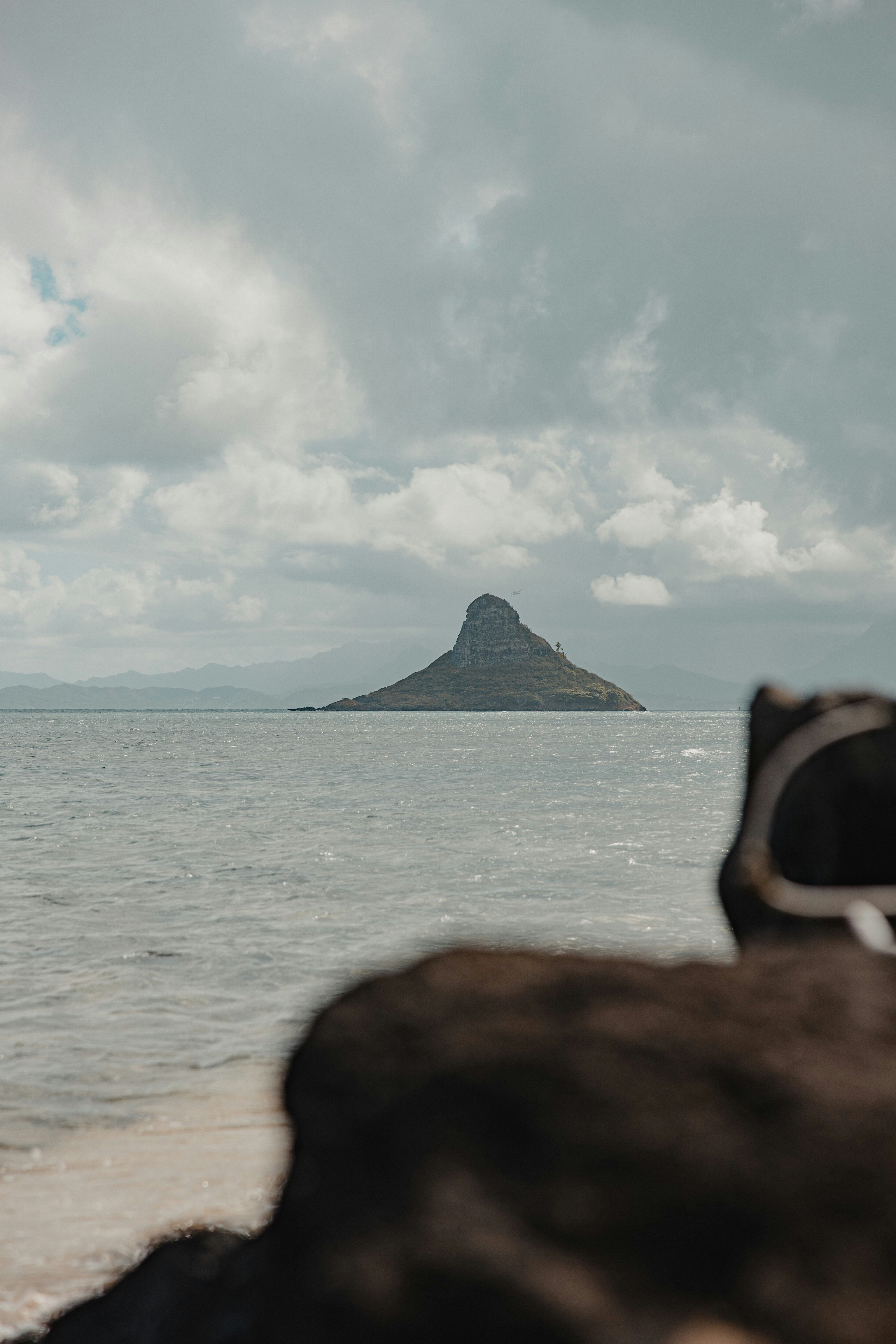 中に白い雲の下で海の前の岩の上に座っている黒いサングラスをかけた人の写真 Unsplashで見つけるグレーの無料写真