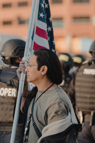 A group of diverse Americans standing united, holding a flag, symbolizing resistance and protection of freedoms.