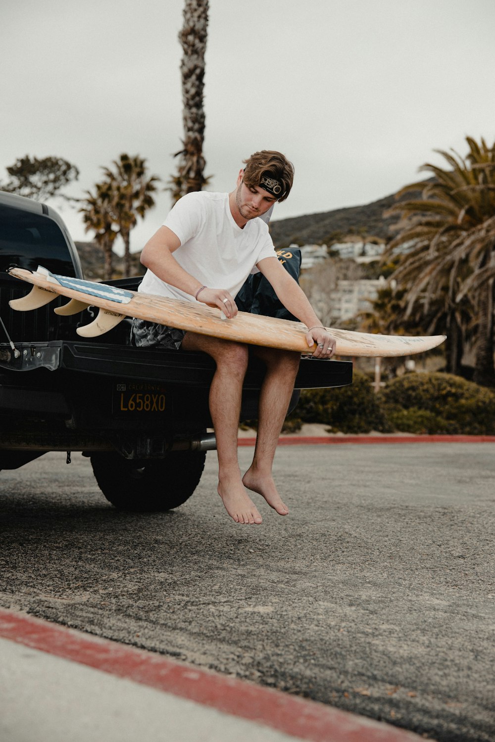 man in white t-shirt and black shorts sitting on black car hood during daytime