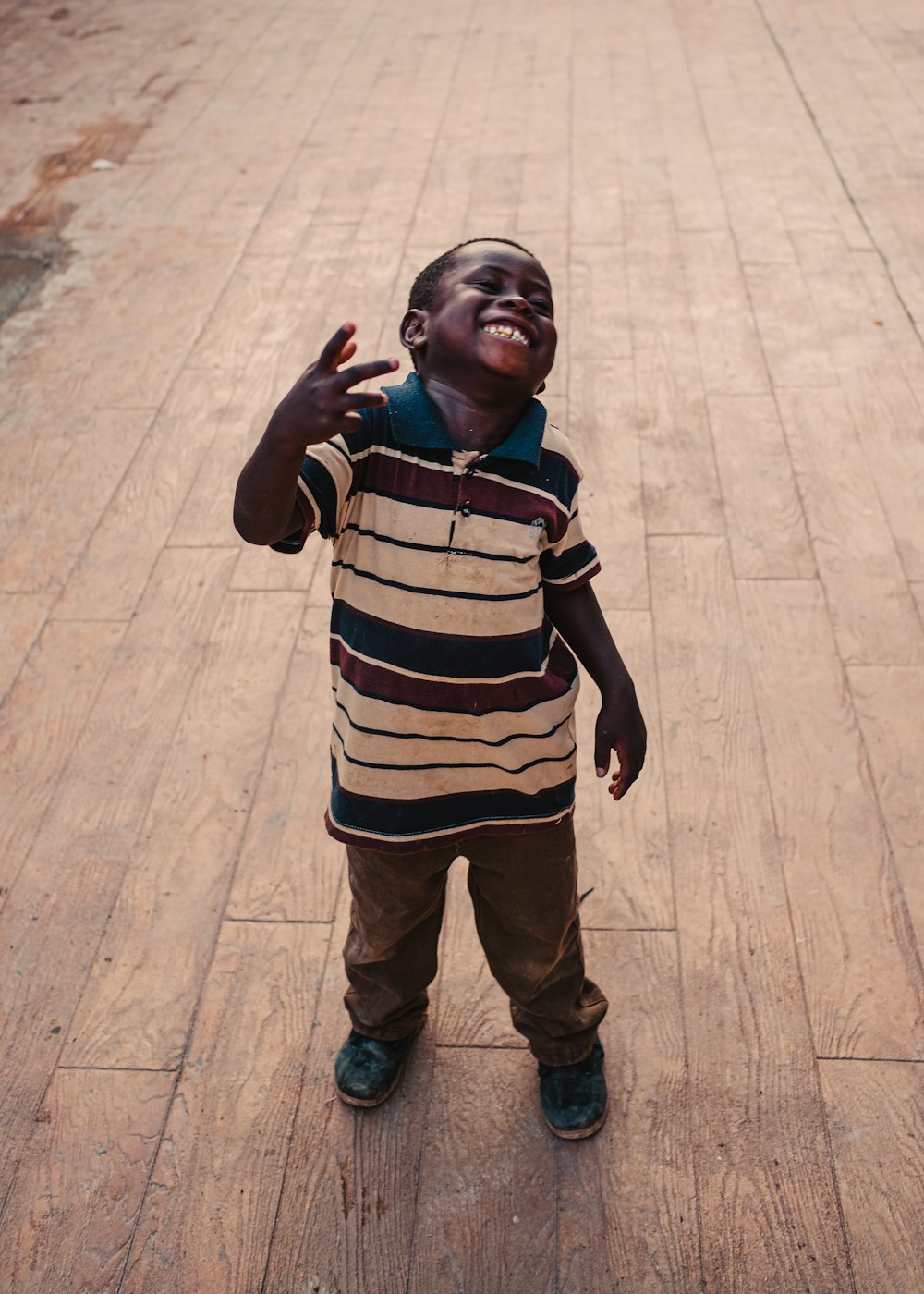 boy in brown white and black striped long sleeve shirt standing on brown wooden floor