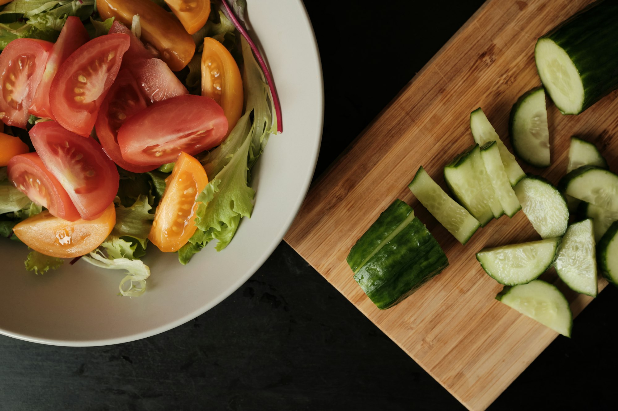 Fresh green salad with cherry tomatoes and sliced cucumber on wooden kitchen board