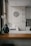 A kitchen interior featuring a modern design with a wooden countertop and a sleek sink. Wall decorations include a larger circular artwork and four smaller plates with artistic designs. An orchid plant and a decorative vase are placed near the window, adding a touch of elegance.