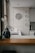 A kitchen interior featuring a modern design with a wooden countertop and a sleek sink. Wall decorations include a larger circular artwork and four smaller plates with artistic designs. An orchid plant and a decorative vase are placed near the window, adding a touch of elegance.