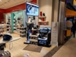 A store display with various home appliances, including vacuum cleaners and irons. The display includes several stacked boxes and products placed on shelves as well as a large digital sign displaying an advertisement. The store is well-lit with a clean, organized layout and there are people in the background near the entrance.