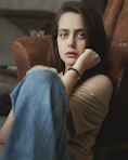 woman in black tank top and blue denim jeans sitting on brown leather couch