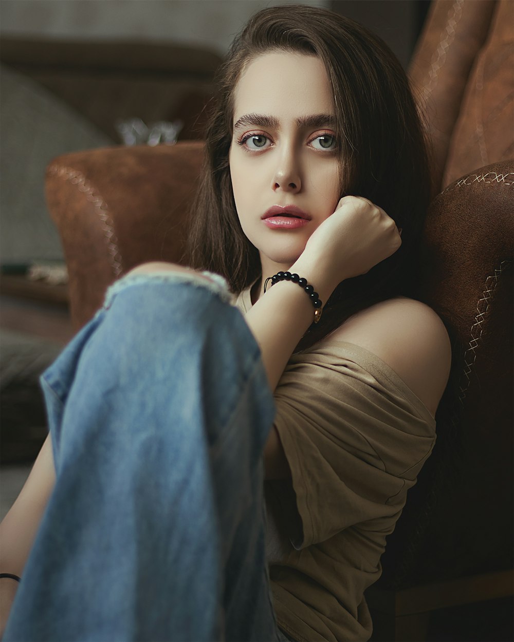 woman in black tank top and blue denim jeans sitting on brown leather couch