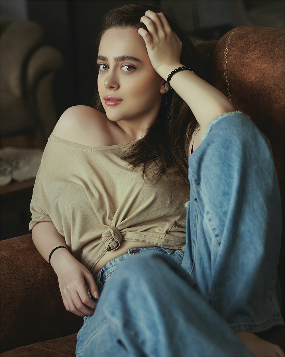 woman in brown crew neck shirt and blue denim jeans sitting on brown sofa