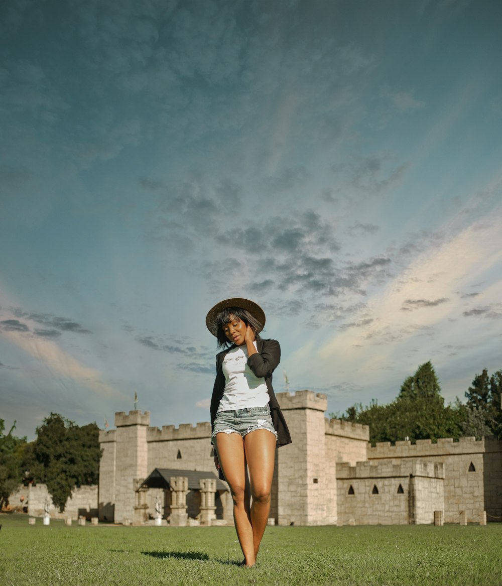 woman in white tank top and blue denim shorts standing on gray concrete floor under blue