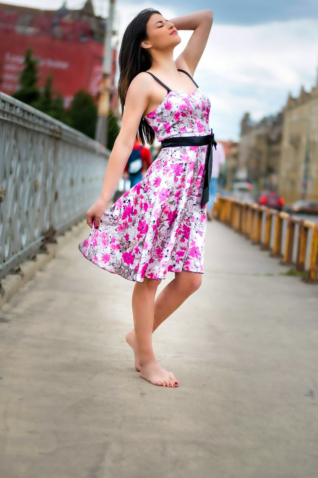 woman in pink and white floral spaghetti strap dress walking on gray concrete bridge during daytime