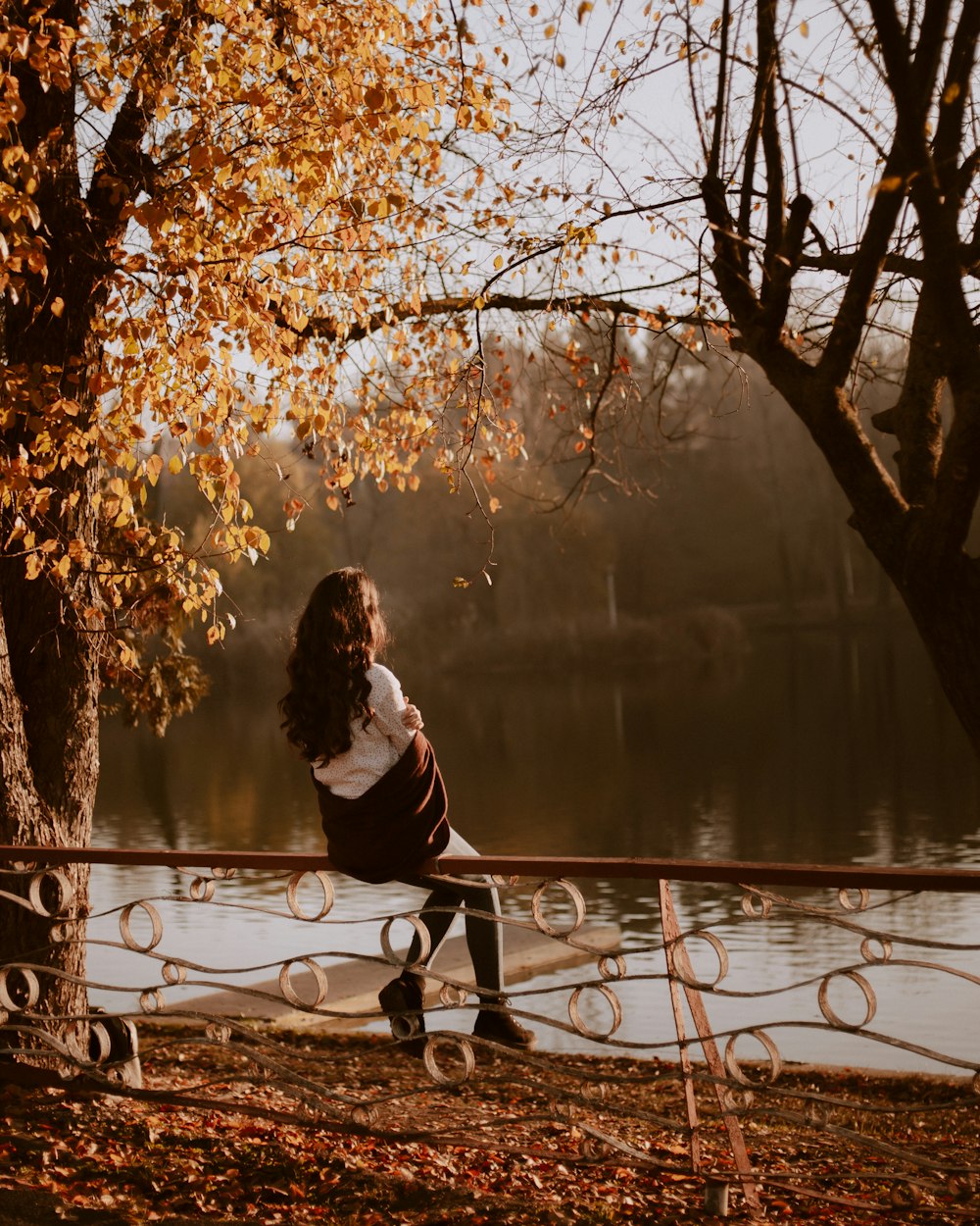 woman in white long sleeve shirt sitting on bench near body of water during daytime