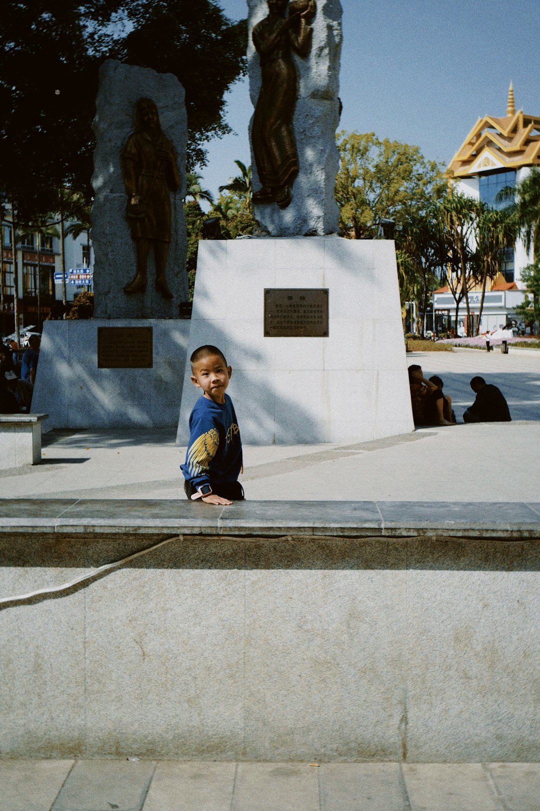 boy in blue jacket sitting on gray concrete bench during daytime