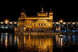 A serene nighttime view of Shri Khatu Shyam Mandir illuminated with golden lights against a deep black sky.