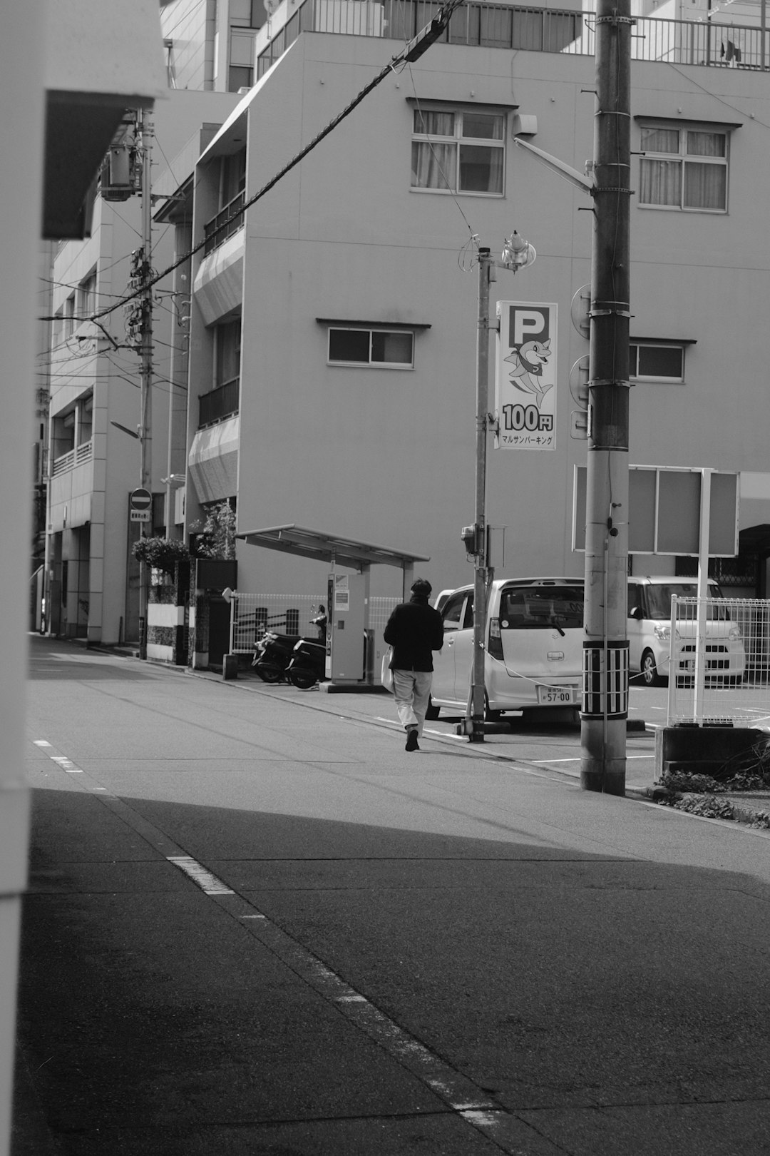 grayscale photo of man walking on sidewalk near traffic light