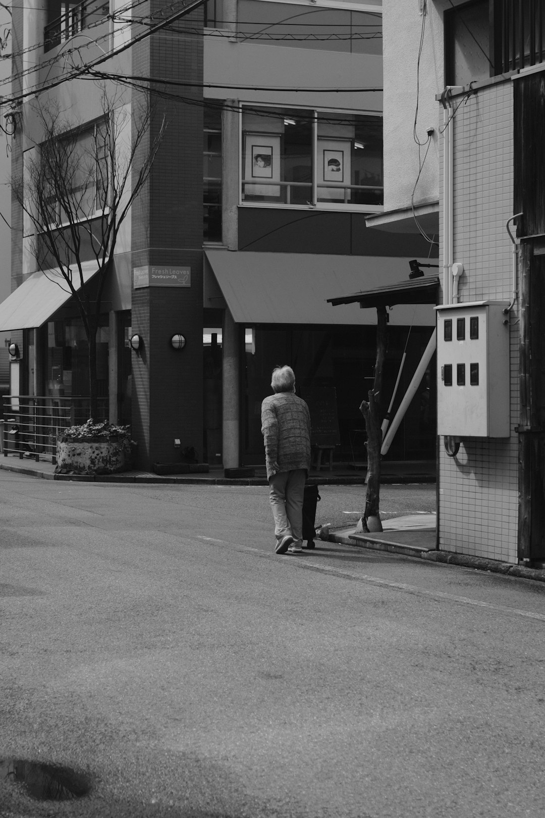 grayscale photo of man walking on sidewalk near building