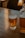 A glass of light beer with foam at the top, labeled with 'Upward Brewing Company', sits on a wooden table. To the right of the glass, there is a transparent pitcher with a similar light beer. The background includes softly lit furniture, creating a cozy atmosphere.