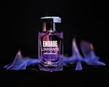 A bottle of perfume labeled 'ENGAGE L'AMANTE Sunkissed' stands against a dark background, surrounded by blue-purple flames that create a dramatic and bold atmosphere.