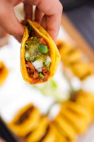 A hand holding a carnitas taco topped with chopped onions and cilantro, ready to take a bite.