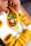 A hand holds a taco filled with ingredients like diced onions, cilantro, and a green salsa. The taco shell is yellow and crispy, and the filling appears to contain seasoned meat.